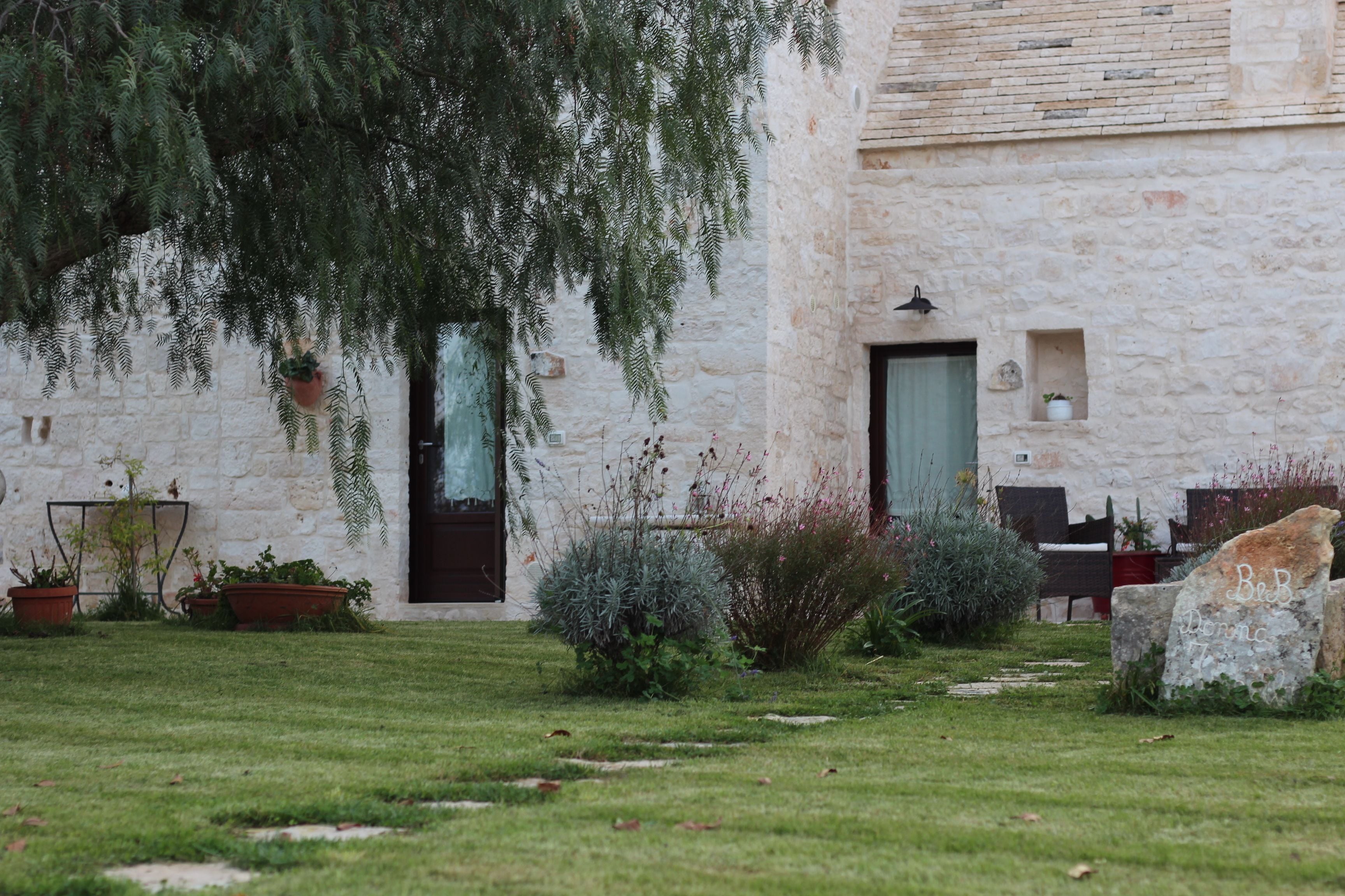 A stone building with a garden in front, including a pathway and potted plants.