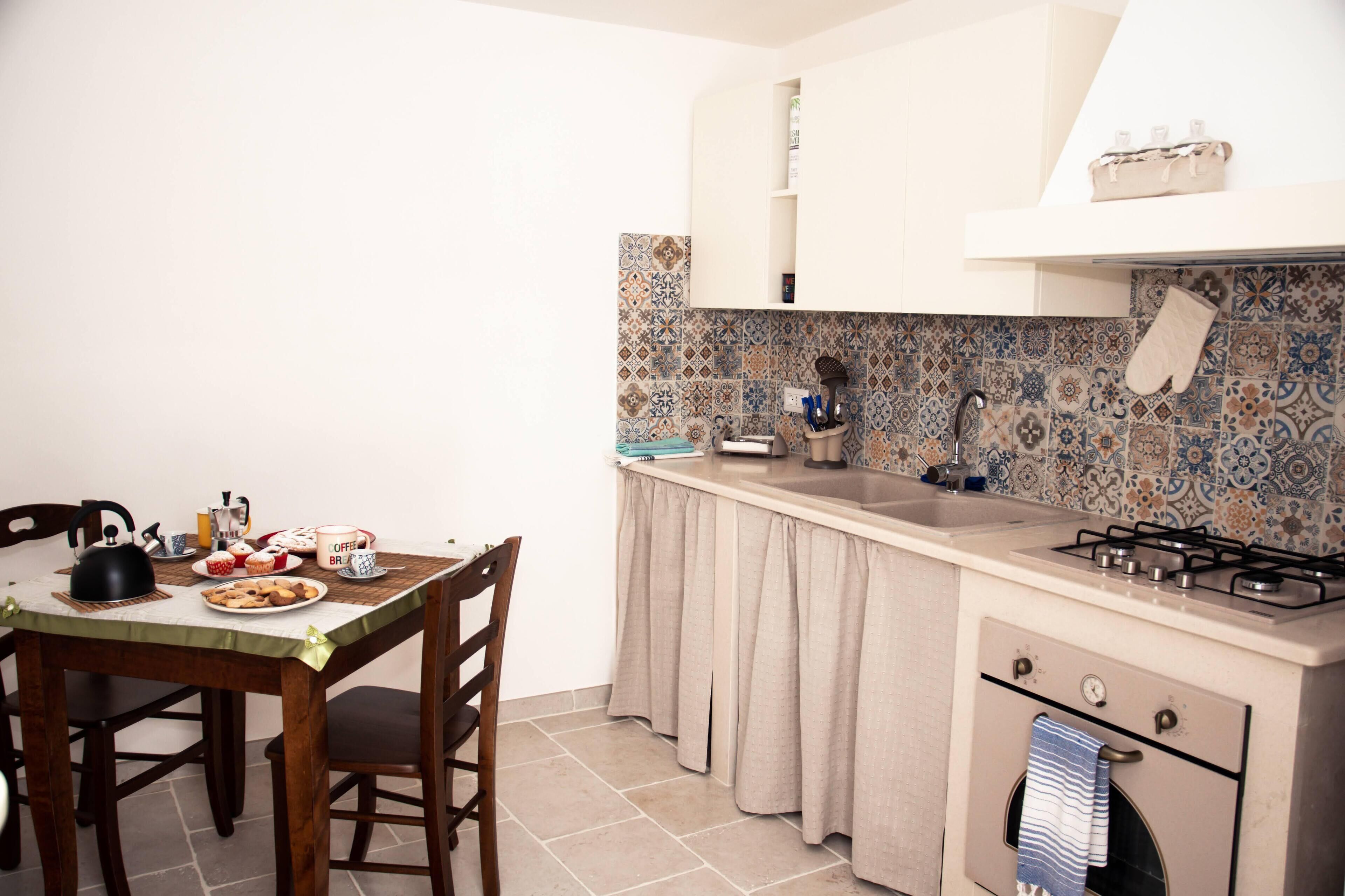 Una cocina compacta con una mesa de comedor, sillas, estufa a gas y un salpicadero de azulejos.