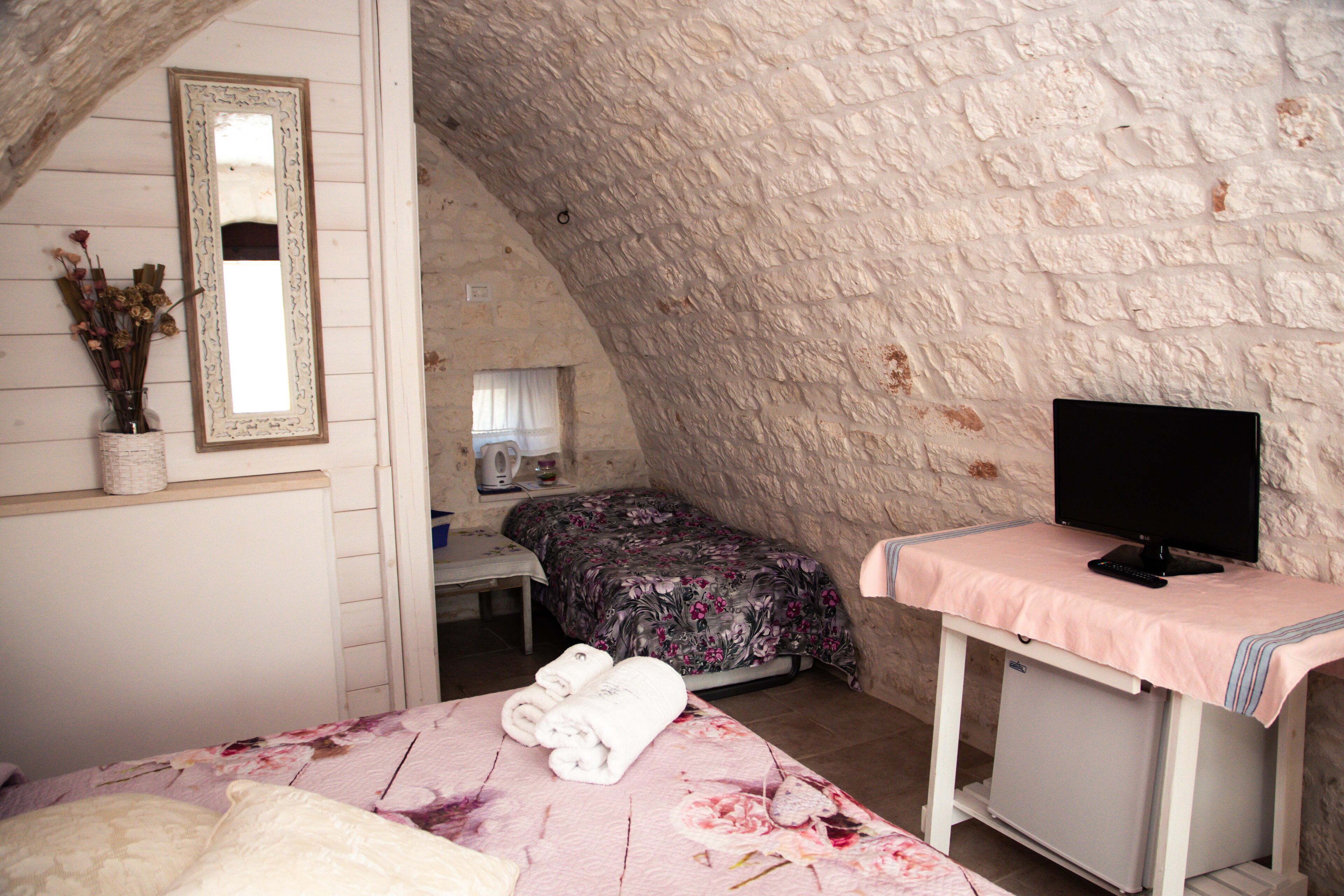 A bedroom with a bed, a desk, a mirror, and a television on a stand.