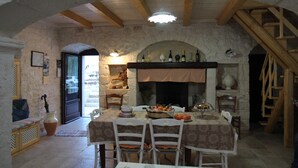 An interior with a stone fireplace, wooden beams, and a dining table set for four. - Trulli Donna Isabella (Locorotondo)