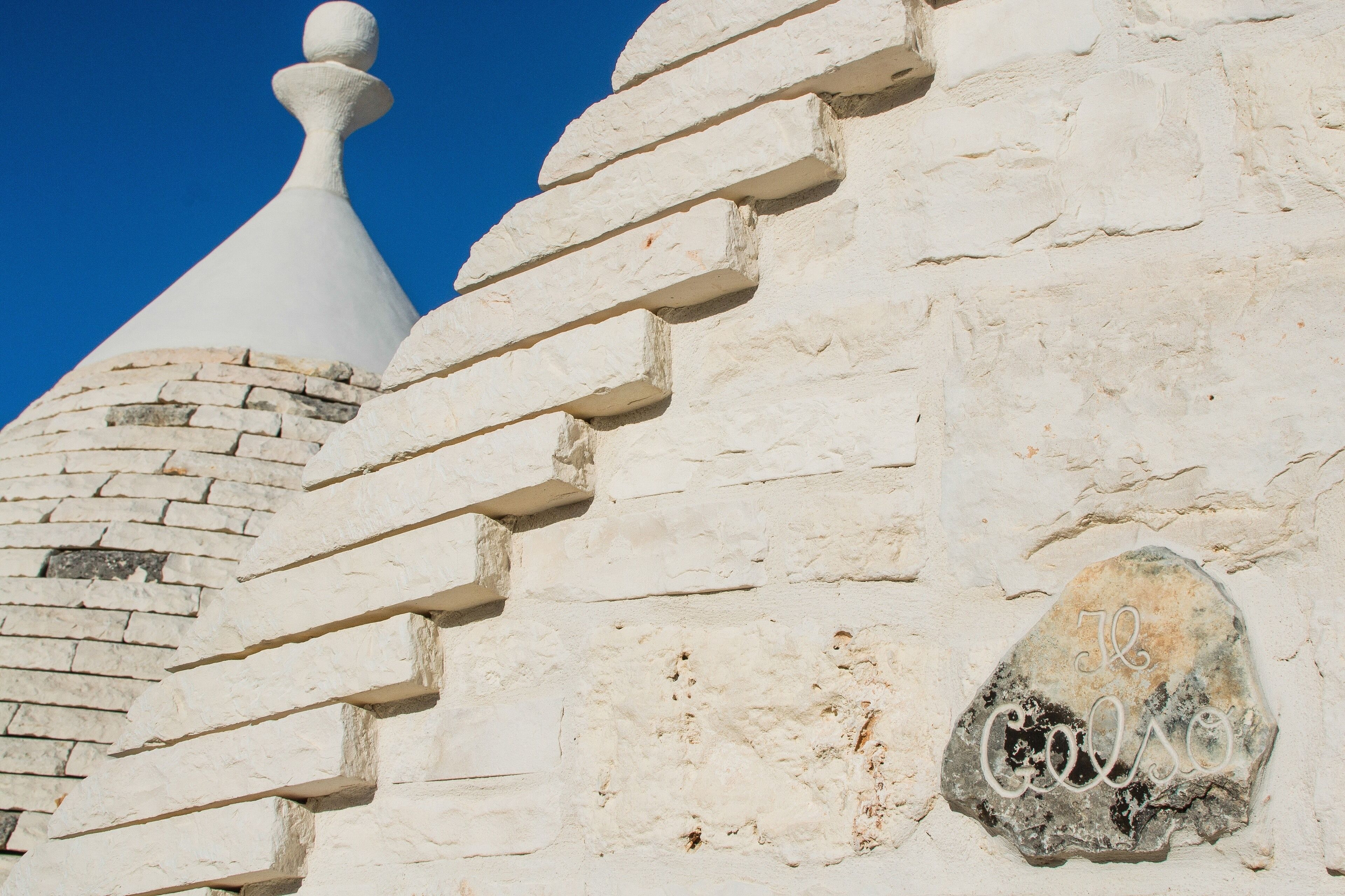 A white brick wall with a stone plaque and a white conical roof.