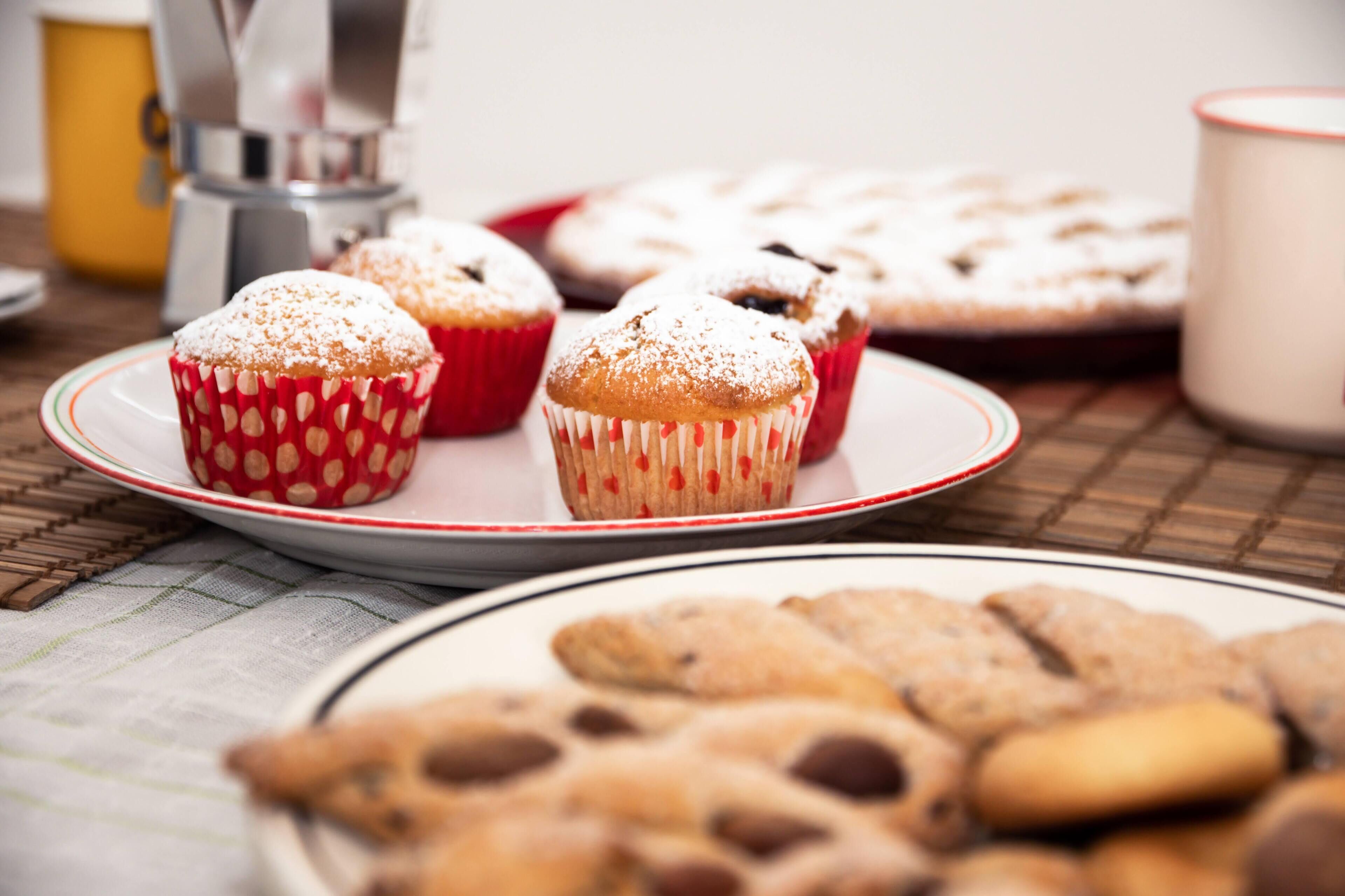 Uma mesa com doces, incluindo muffins e bolachas, em pratos.