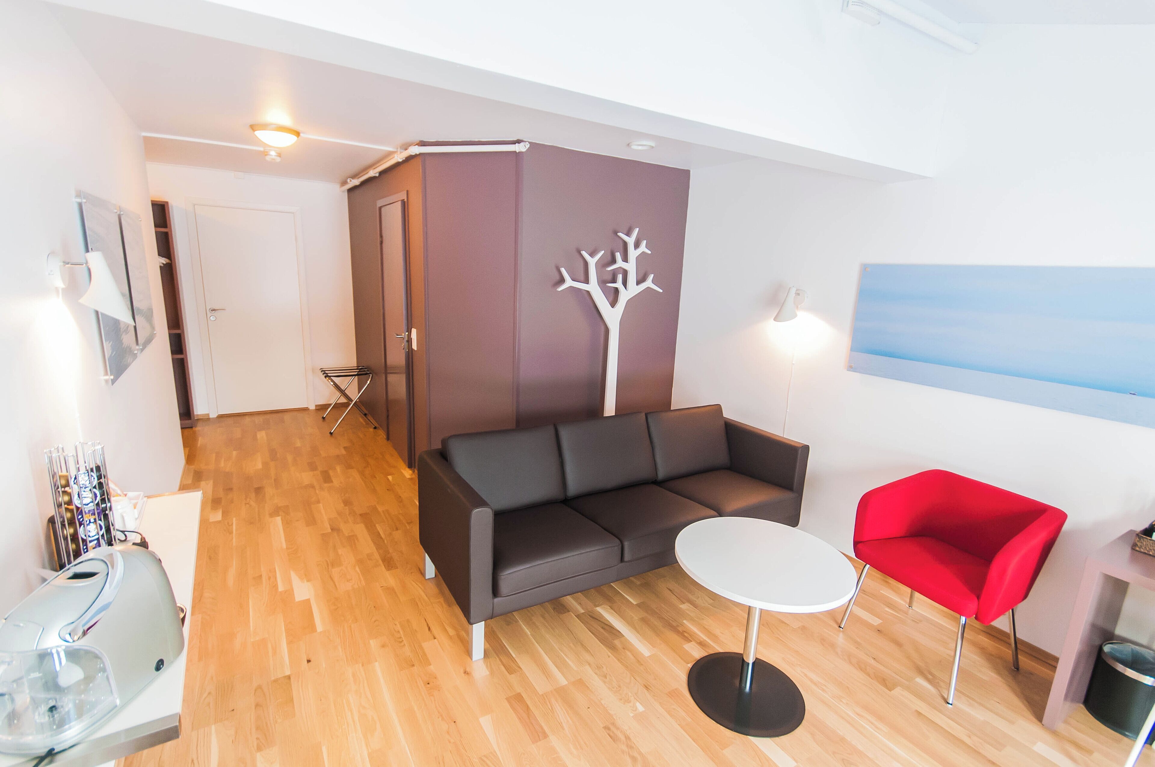 Ett modernt vardagsrum med en mörkgrå soffa, en röd fåtölj och ett litet vitt bord. En vit julgransprydnad är upphängd på väggen, och ovanför soffan hänger en tavla.