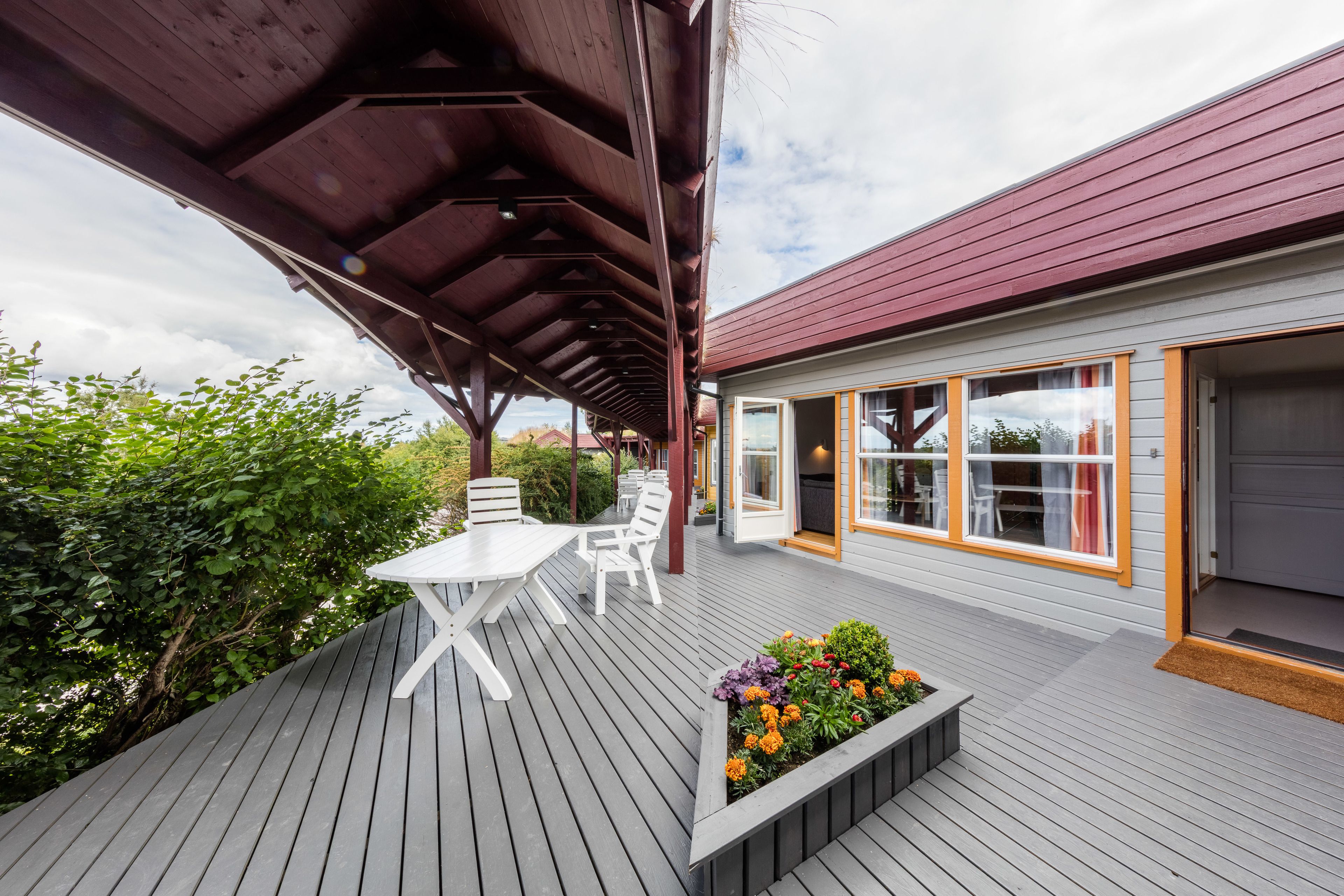 A covered outdoor deck with a table and chairs, a flower planter, and a house with large windows and a garage.