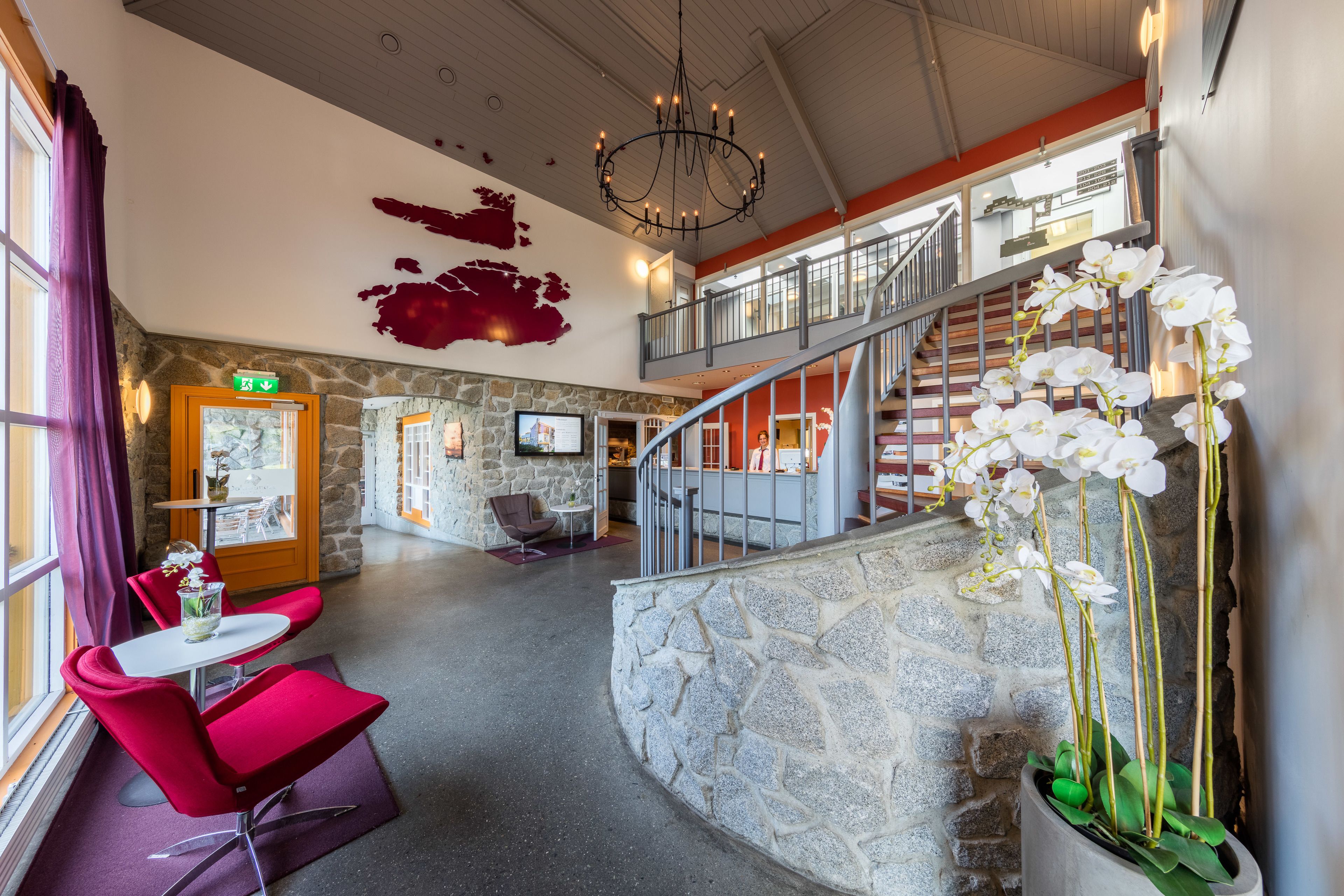 A spacious lobby with a stone wall, a staircase, and a seating area with red chairs.