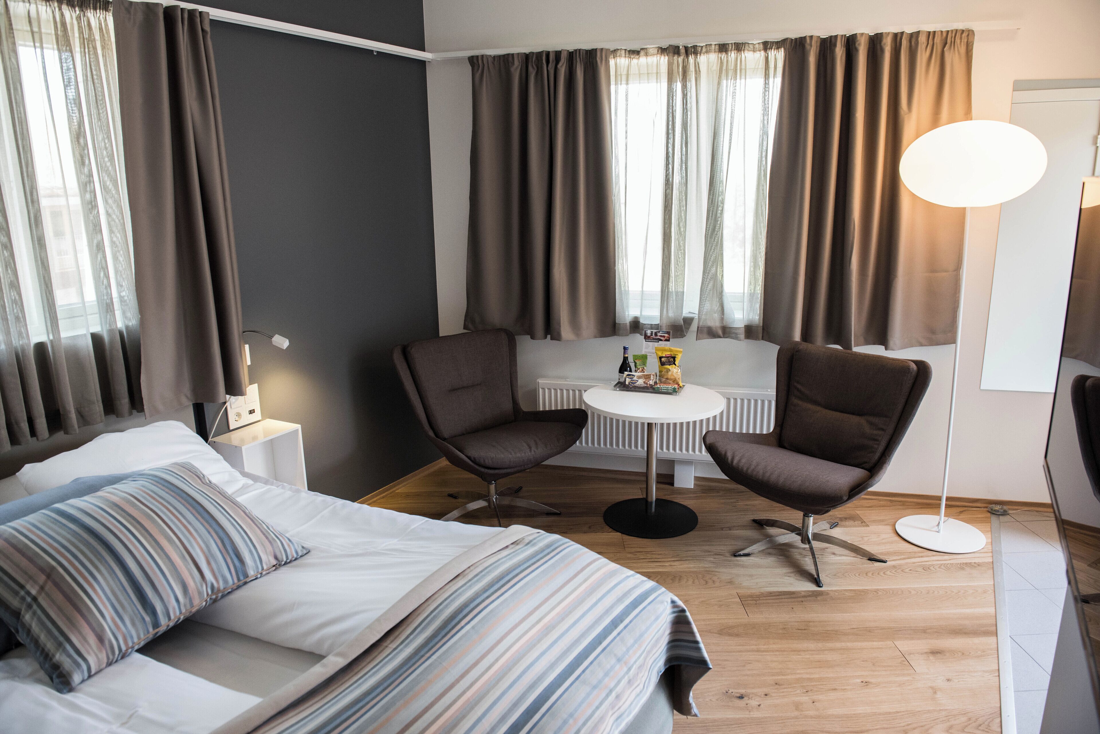 A hotel room with a bed, two armchairs, a small table, and a lamp.