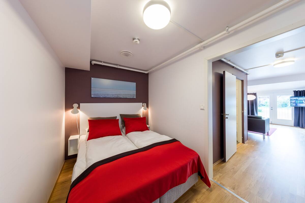 Ein modernes Schlafzimmer mit einem Bett, Nachttischlampen und Blick auf einen Wohnbereich.