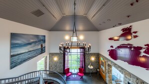 A spacious room with a high ceiling, a large painting of a seascape, a chandelier, two red chairs, and a stone wall with a map. - Dolmsundet Hotell Hitra (Hitra)