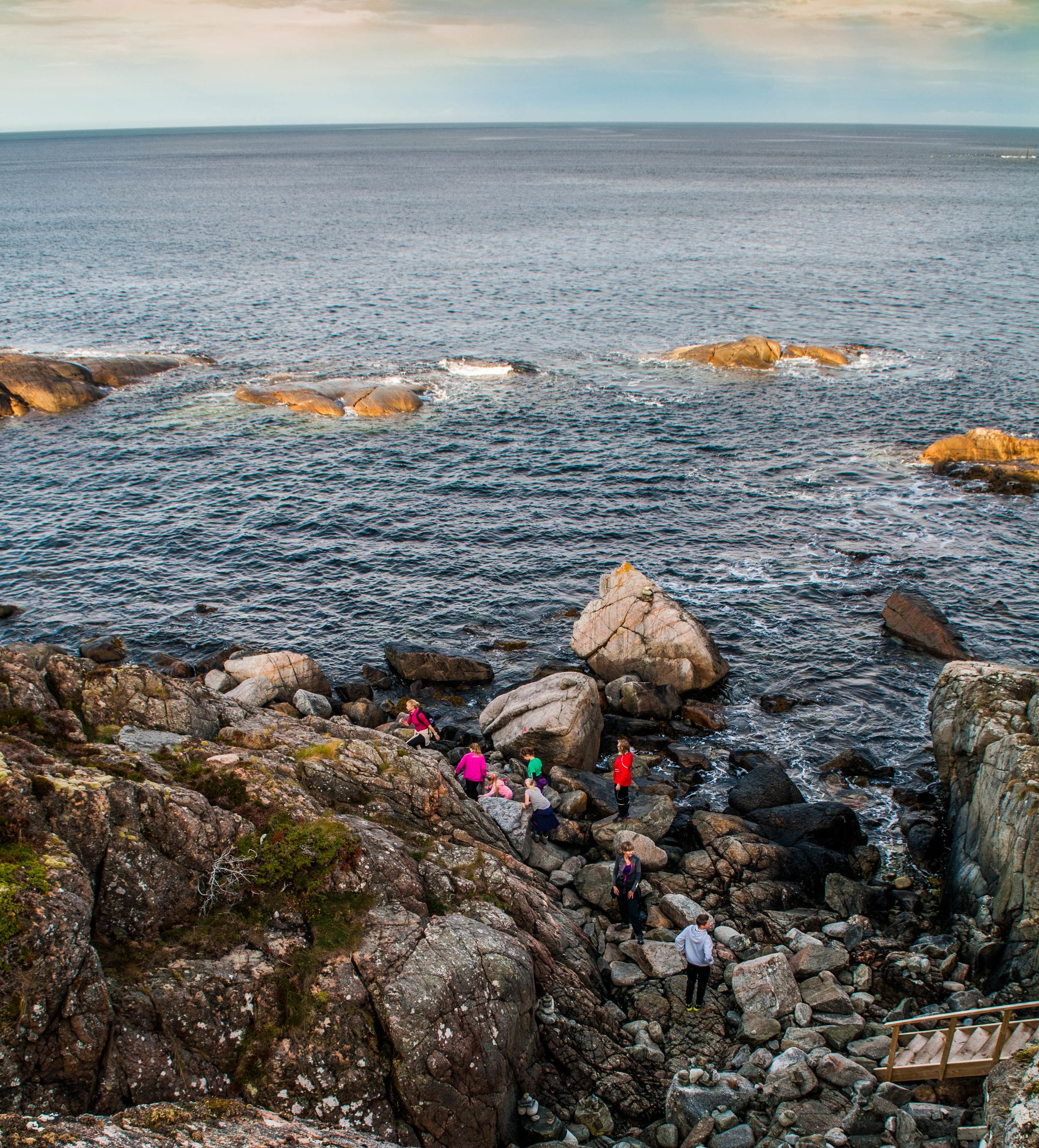 A rocky coastal area with people walking on the rocks and a wooden walkway.