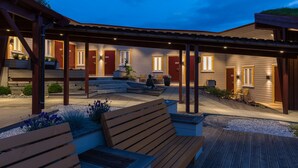 A covered outdoor area with wooden benches and planters, a stone pathway, and a building with numbered doors. - Dolmsundet Hotell Hitra (Hitra)