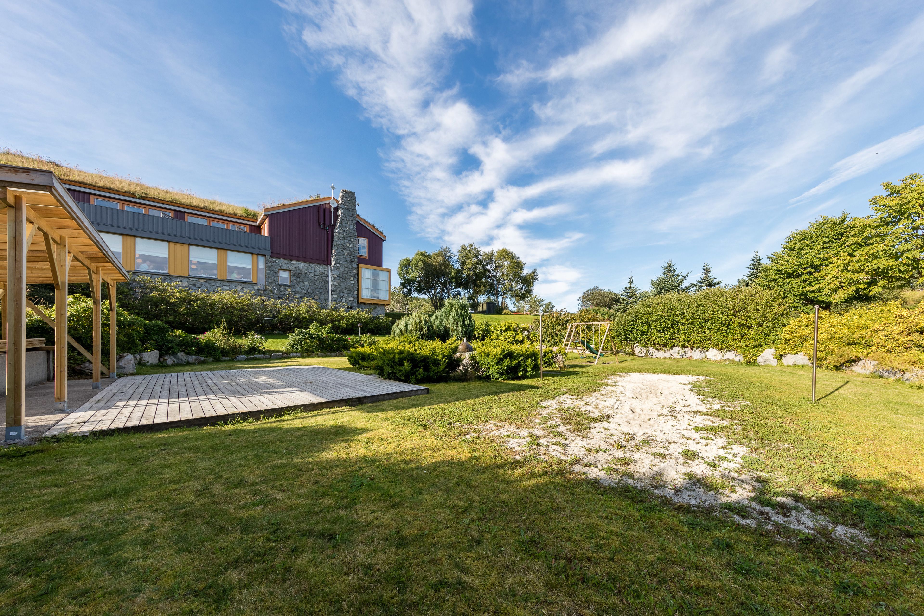 Una casa moderna con terraza de madera, paredes de piedra y un jardín bien cuidado.