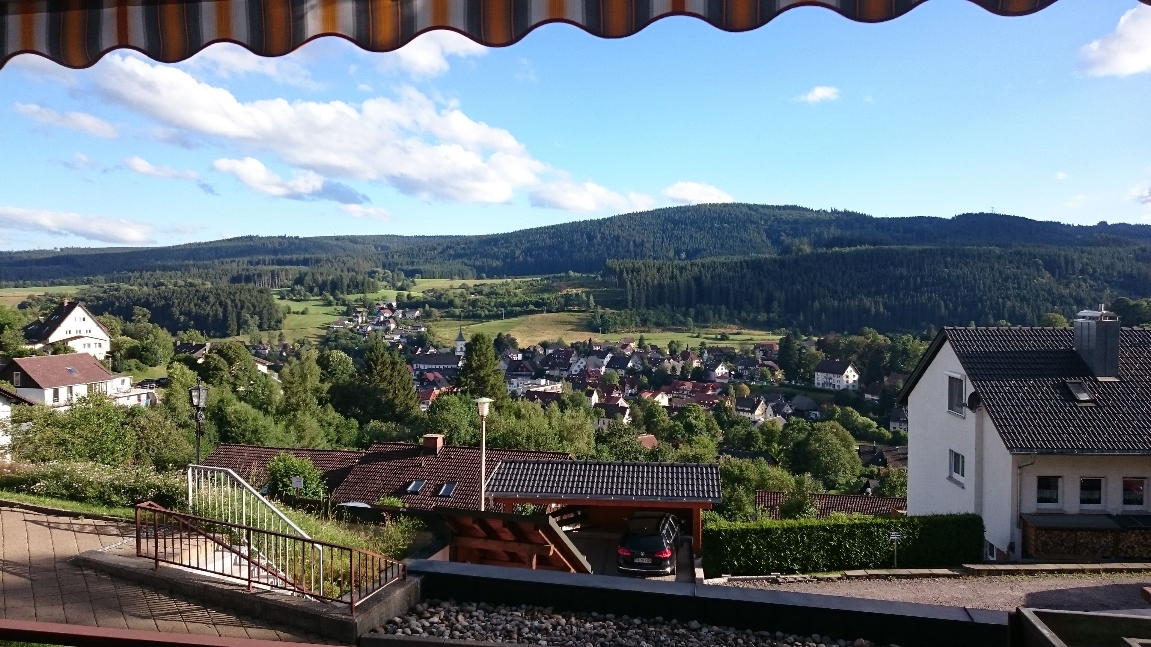 Une vue pittoresque d’un village avec ses maisons traditionnelles, une voie ferrée et les collines verdoyantes qui l’entourent.