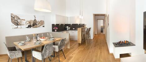A modern kitchen with a dining area, wooden flooring, and a view into the living room.