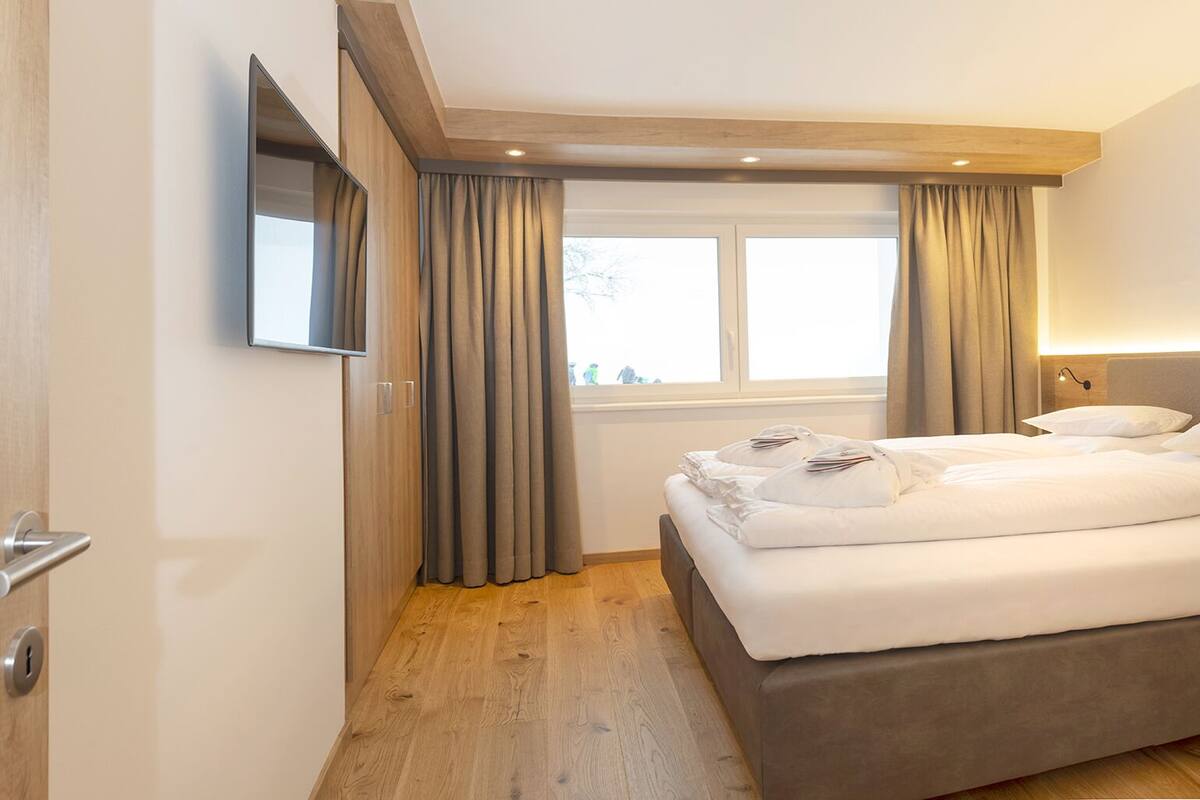 Une chambre d’hôtel moderne, équipée d’un lit, d’une table de chevet, d’un téléviseur fixé au mur et d’une fenêtre avec des rideaux.