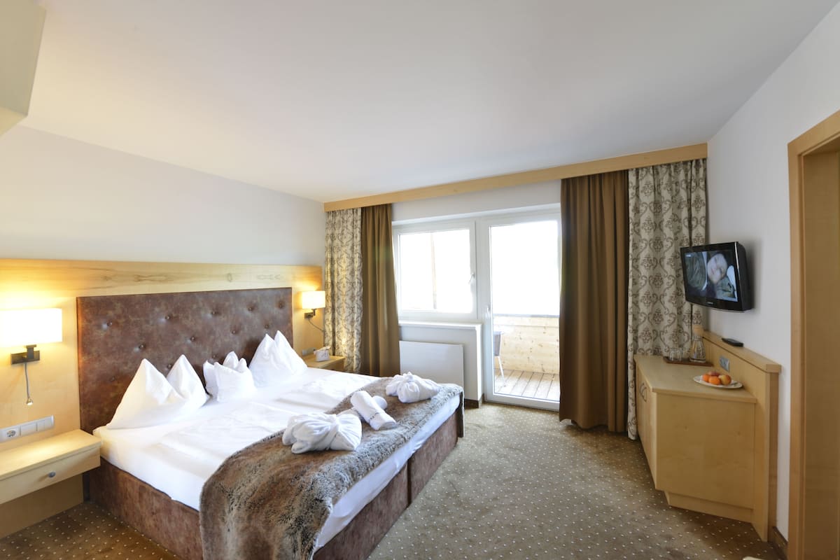 Une chambre d’hôtel avec un grand lit, une table de chevet avec une lampe, un téléviseur posé sur un meuble et une vue sur l’extérieur grâce à une porte-fenêtre coulissante.