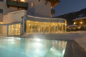 Un espace piscine extérieure chauffé, doté de murs en verre, avec un paysage enneigé en arrière-plan.