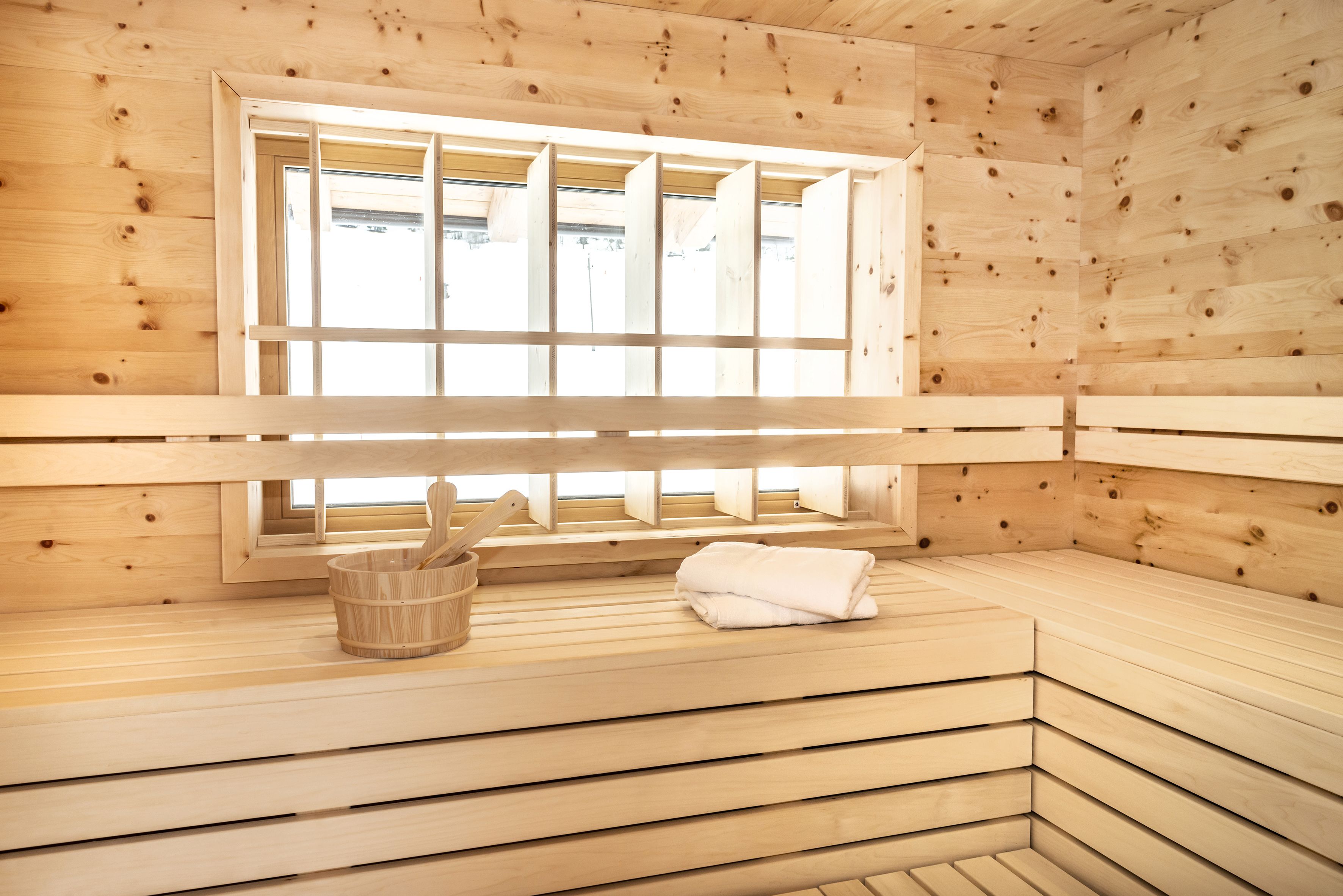 Una sauna con pareti e panche in legno, una finestra con persiane e un catino di legno.
