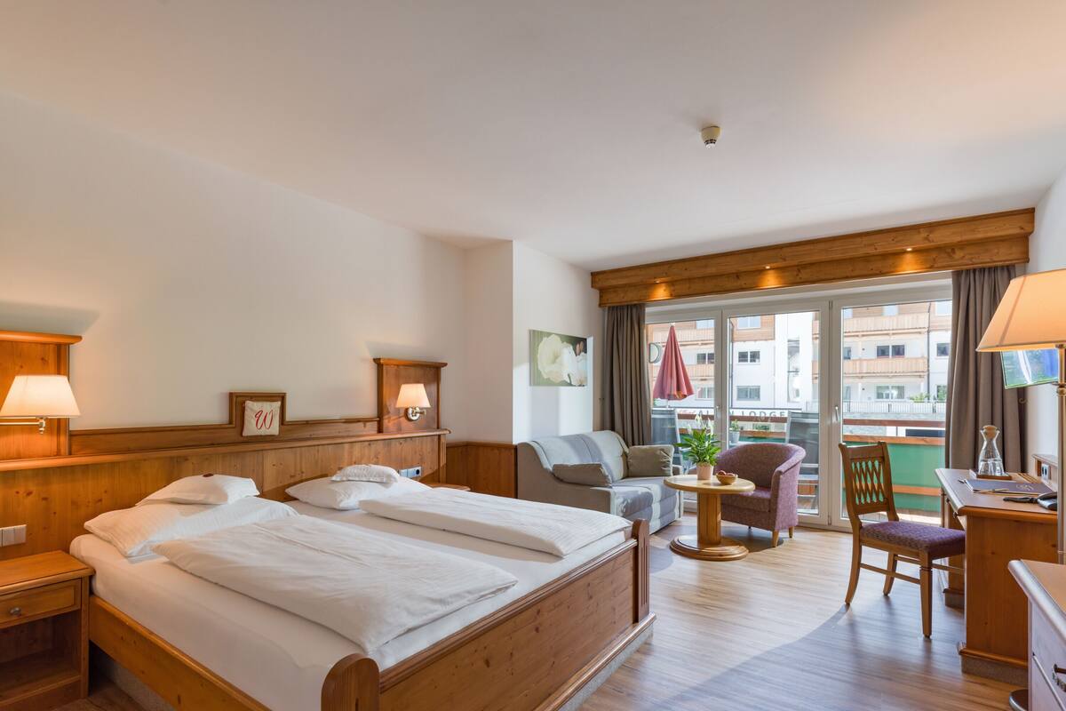 Une chambre d’hôtel avec un grand lit, un bureau, une chaise et un balcon donnant sur des immeubles.