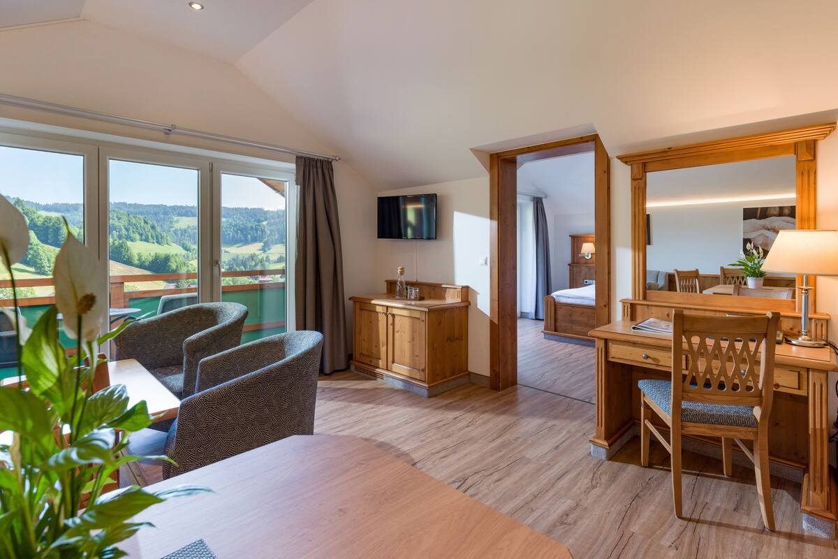 Une chambre d’hôtel avec un balcon, des meubles en bois, une télévision et un coin repas.