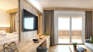 Een hotelkamer met een bed, een bureau met telefoon, een flatscreen televisie, een bank en een balkon met houten hekwerk.