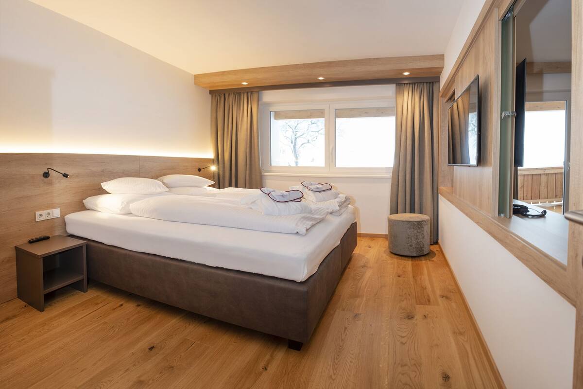 Une chambre moderne avec un grand lit, des tables de chevet, une télévision et une fenêtre avec des rideaux.