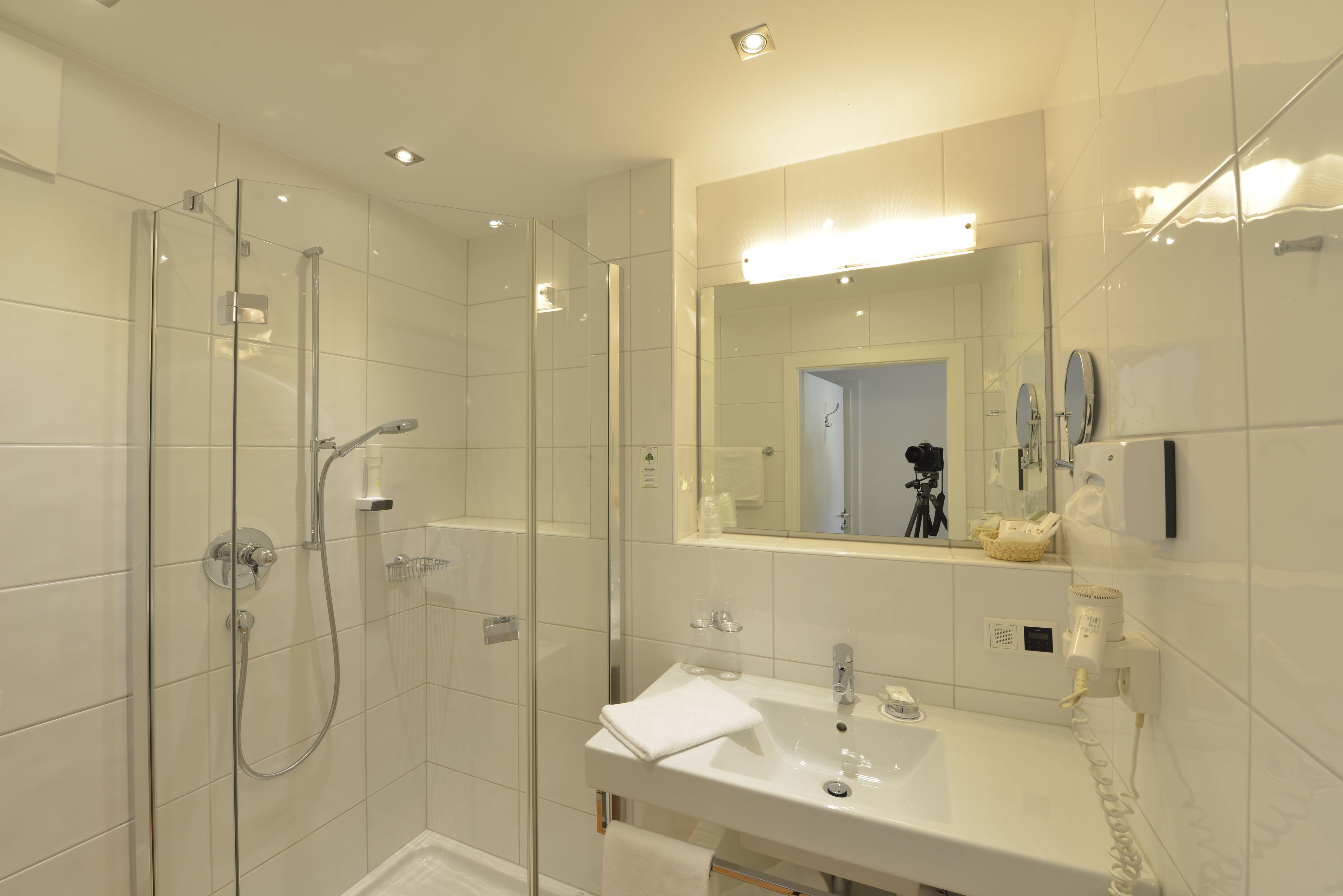 Een moderne badkamer met een douchecabine van glas, een witte wastafel en een grote spiegel.