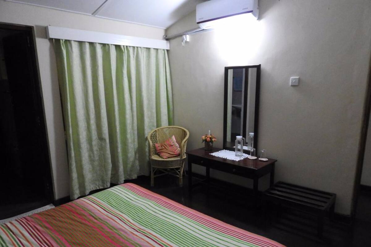 A hotel room with a bed, a chair, a desk, a mirror, and a window with curtains.