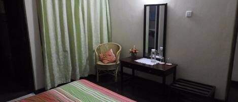 A hotel room with a bed, a chair, a desk, a mirror, and a window with curtains.