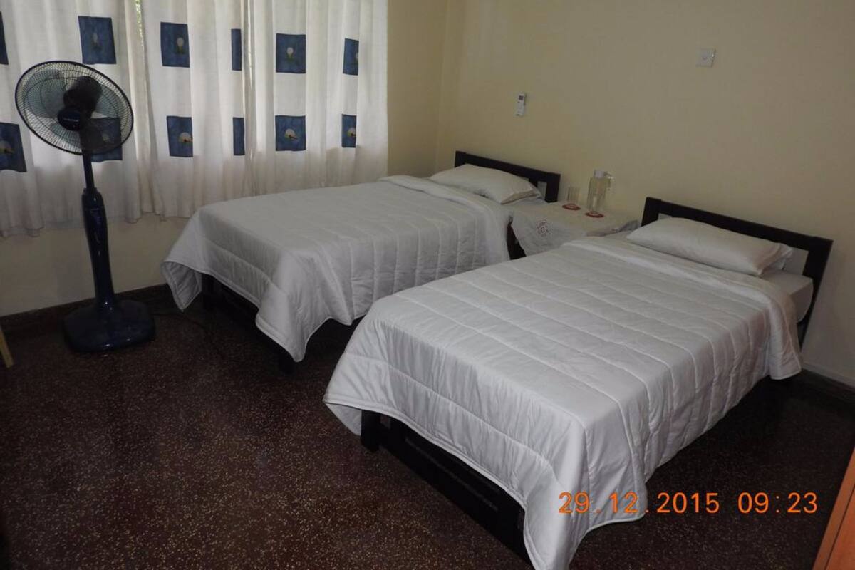 A hotel room with two beds, a standing fan, and a window with curtains.