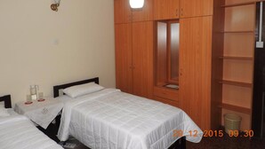 A hotel room with two beds, wooden wardrobe, and a small table with glasses. - Hanthana Breeze Home Stay (Kandy)