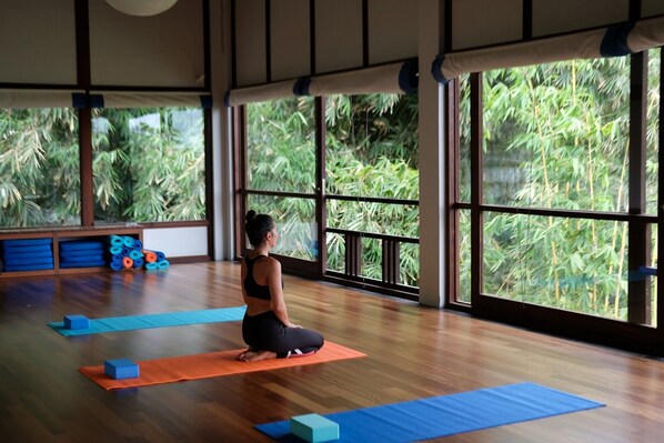 Quarto amplo com janelas grandes, piso de madeira e colchonetes de exercício.