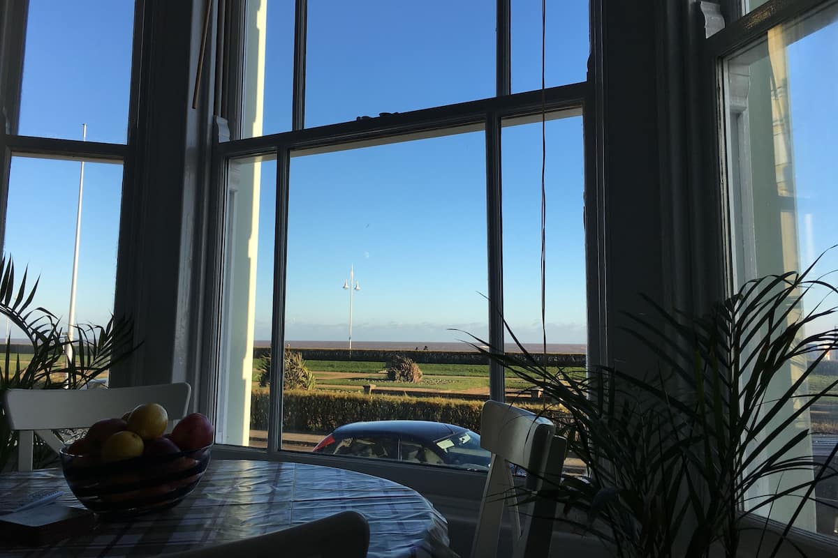 A room with a large window, a table with a bowl of fruit, and a chair.