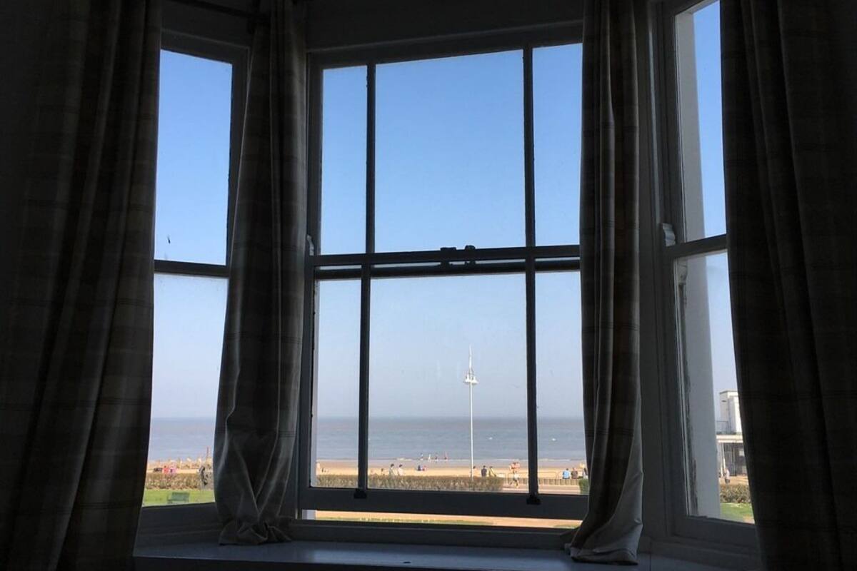 A room with a large bay window overlooking a beach.