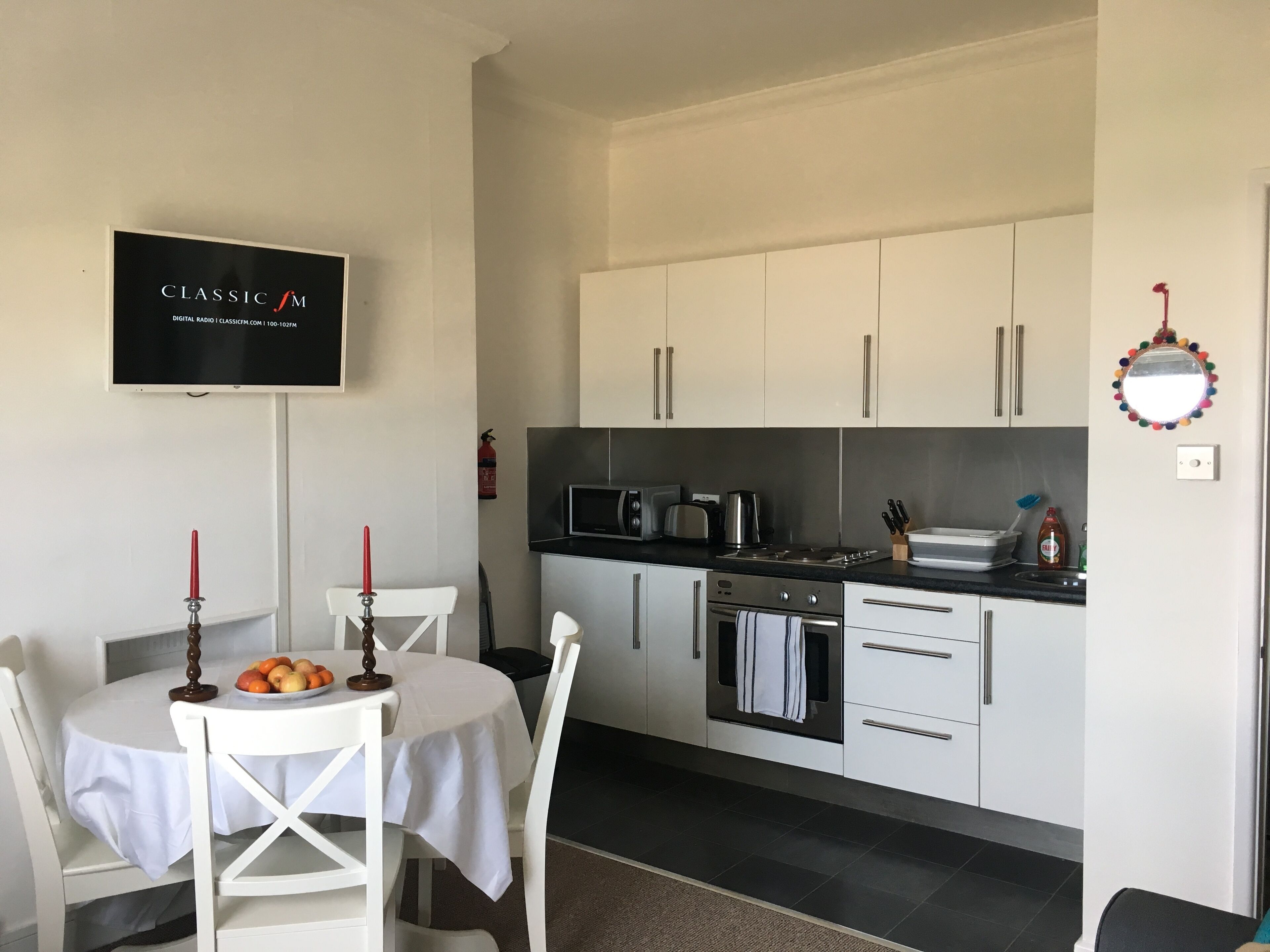 A modern kitchen with white cabinetry, a microwave, a stove, and a sink. There is a table with a white tablecloth and a candle.