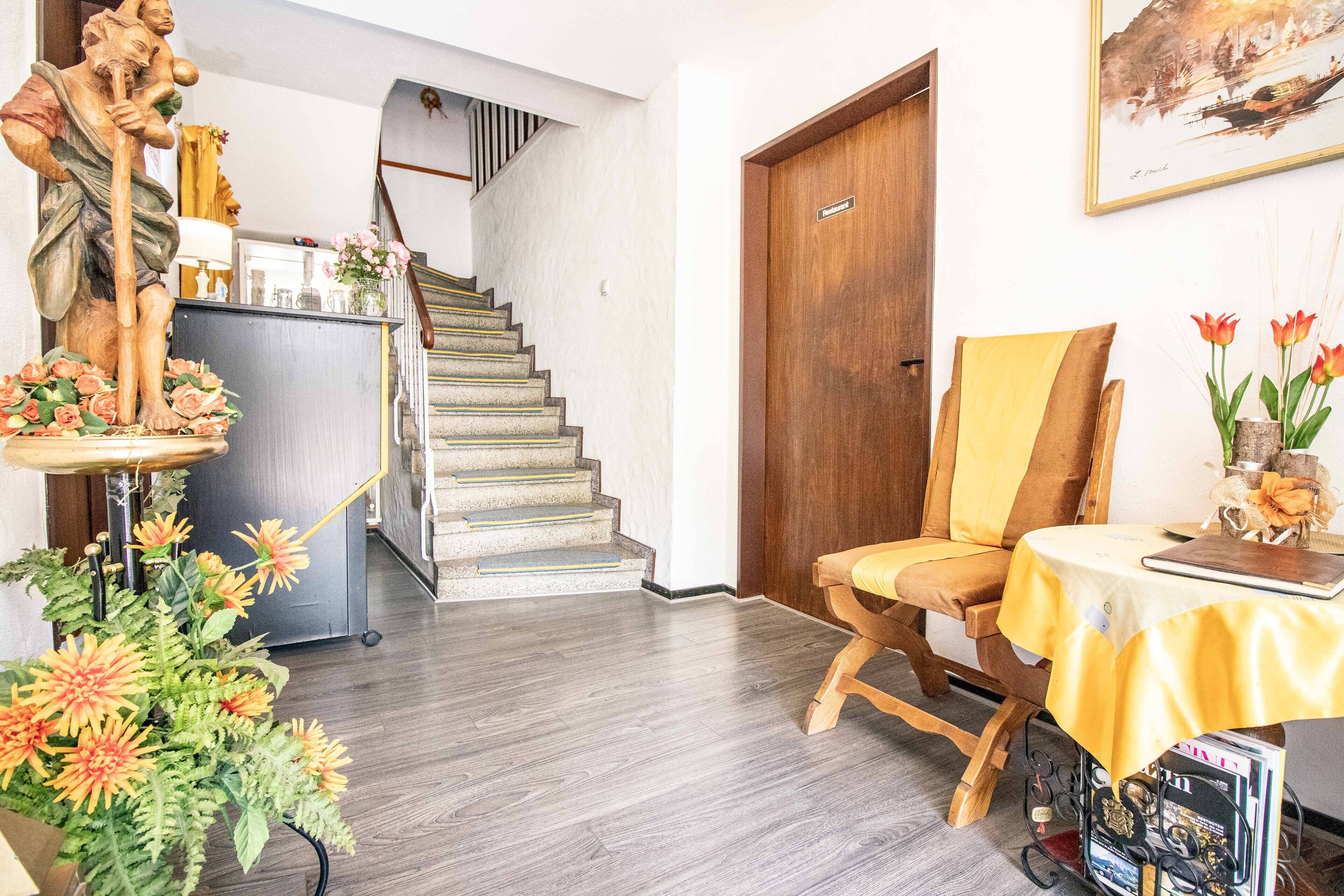 A room with a wooden statue, a chair, a table with a yellow tablecloth, and a staircase leading to another room.