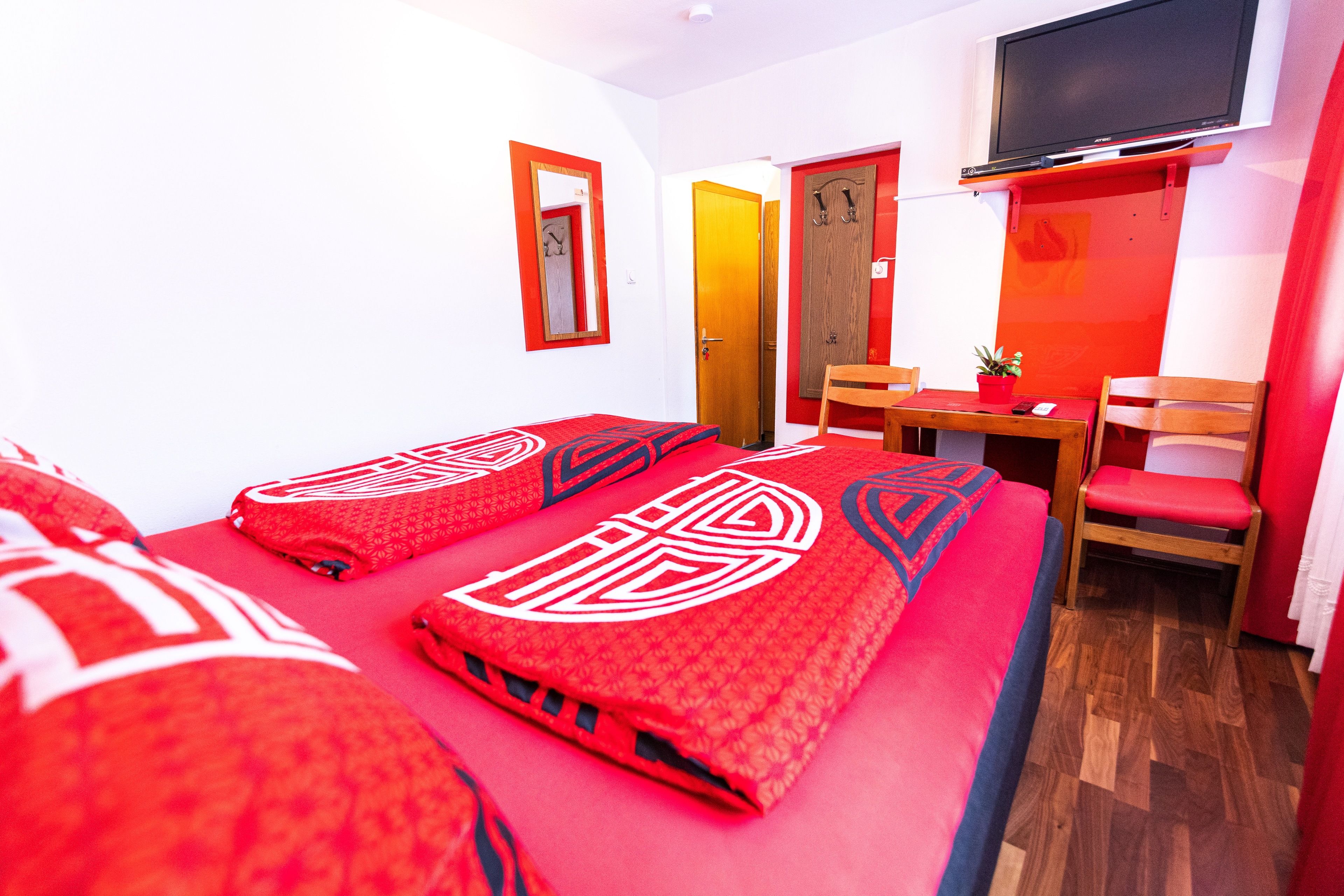 A hotel room with two beds, a desk, a chair, a TV, and a door.