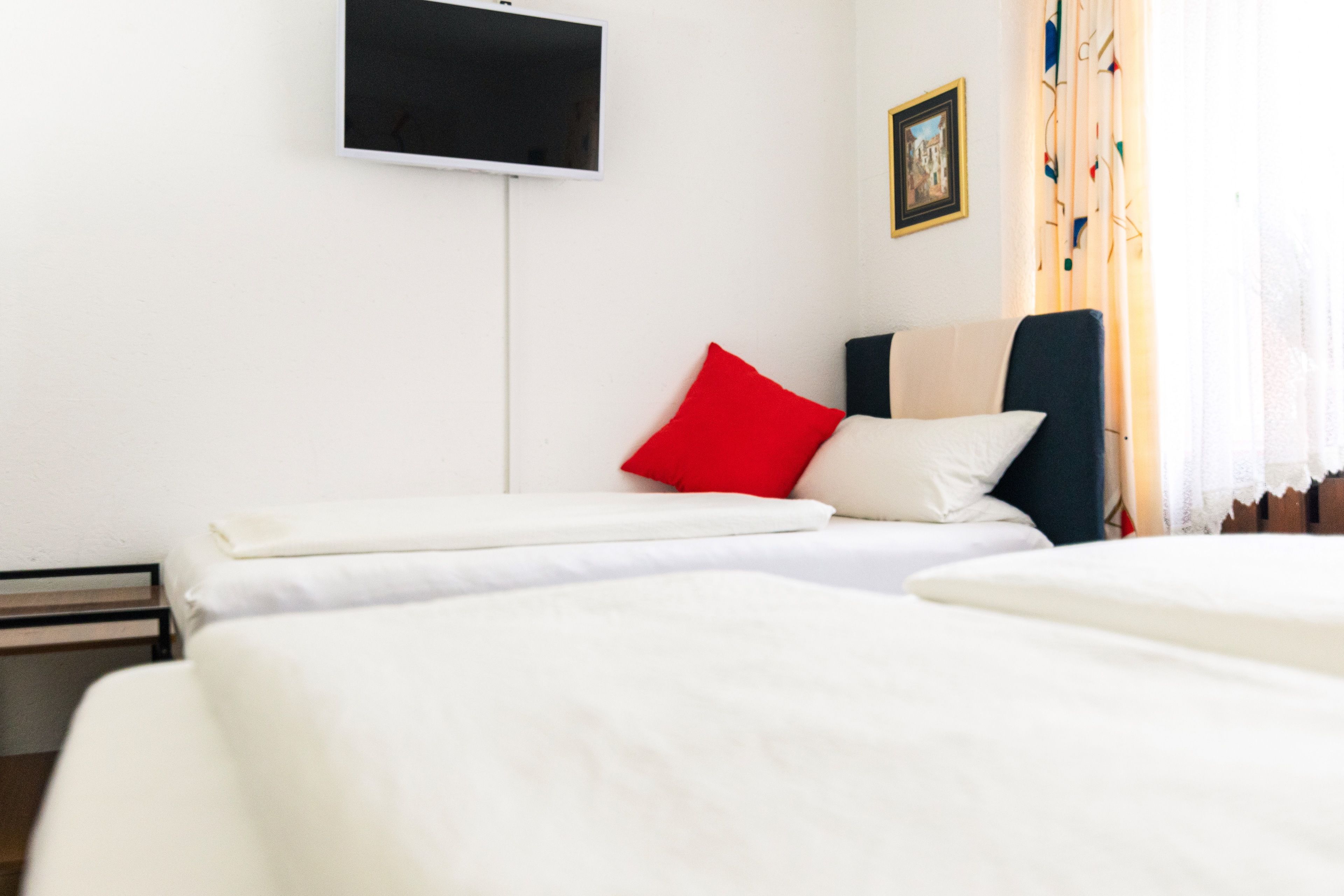 A hotel room with two beds, a flat-screen TV mounted on the wall, and a window with curtains.