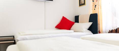A hotel room with two beds, a flat-screen TV mounted on the wall, and a window with curtains.