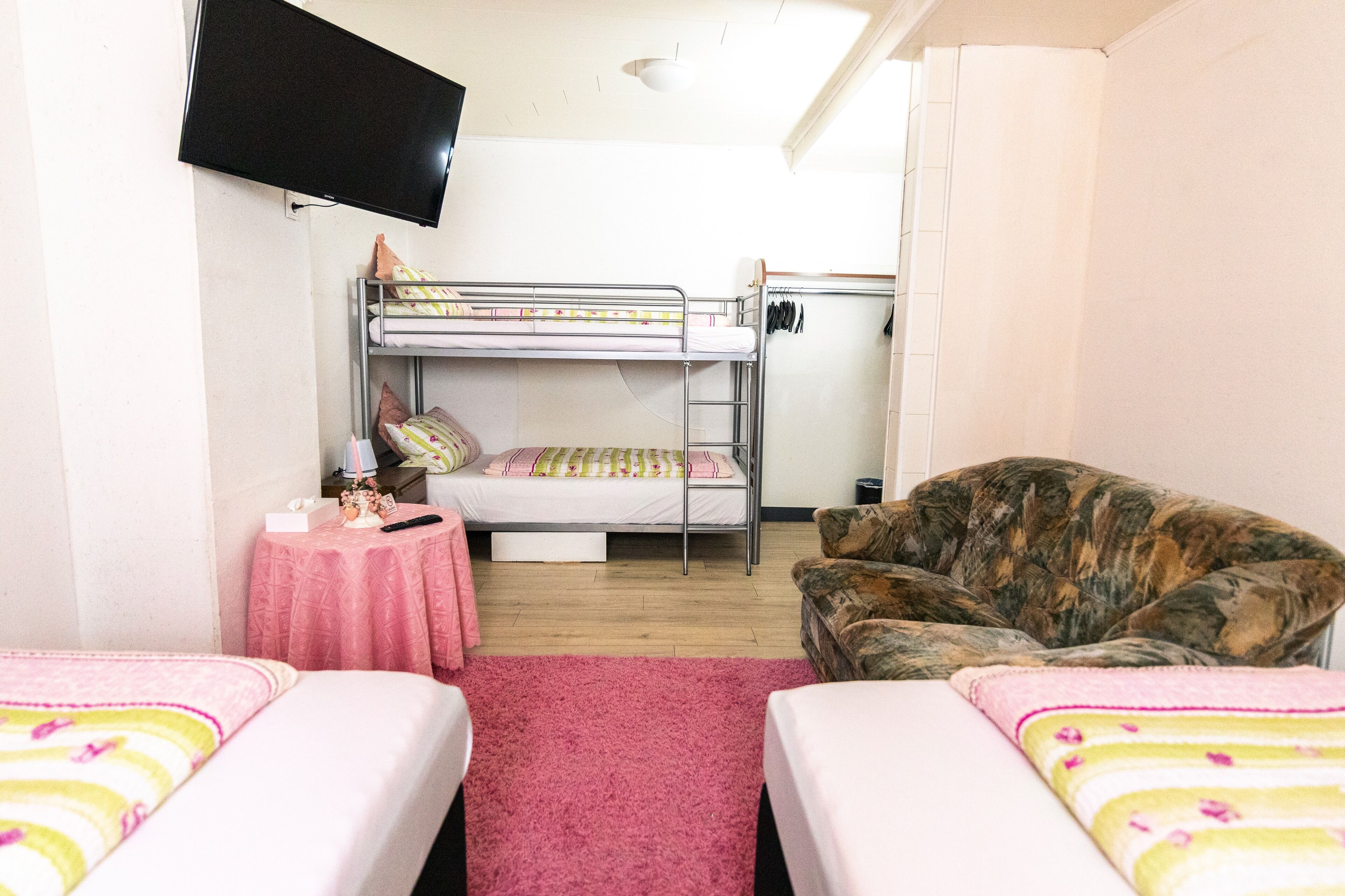 Ein Schlafsaalzimmer mit Etagenbetten, einem Fernseher, einem kleinen Tisch mit rosa Tischdecke und einem Sofa.