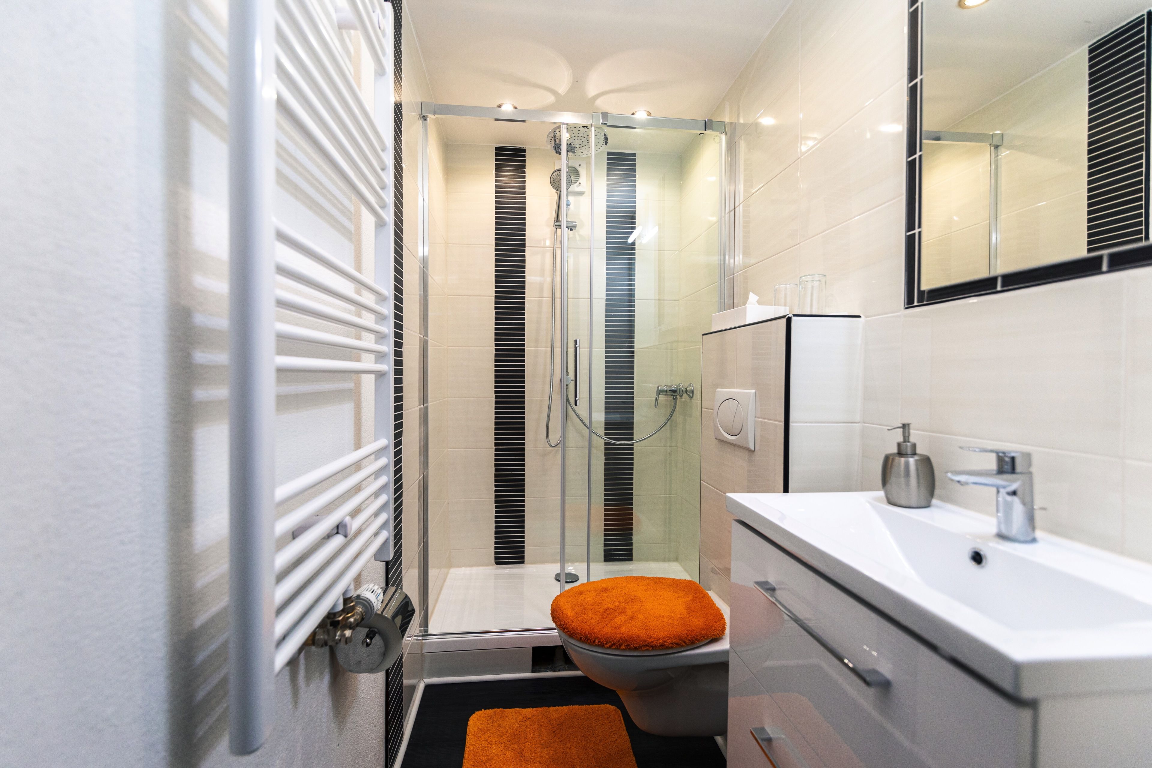 Een moderne badkamer met een douchecabine van glas, een witte wastafel en een toilet met oranje zitting.