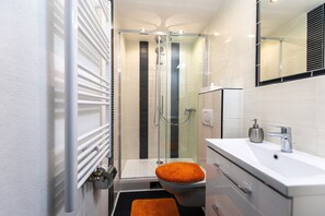 A modern bathroom with a glass-enclosed shower, a white sink, and a toilet with an orange seat. - Gasthaus Tannenhof (Lutz)