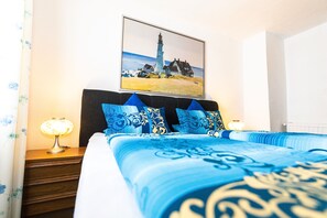 A bedroom with a bed, two bedside tables, a nightstand, a lamp, and a painting of a lighthouse on the wall. - Gasthaus Tannenhof (Lutz)
