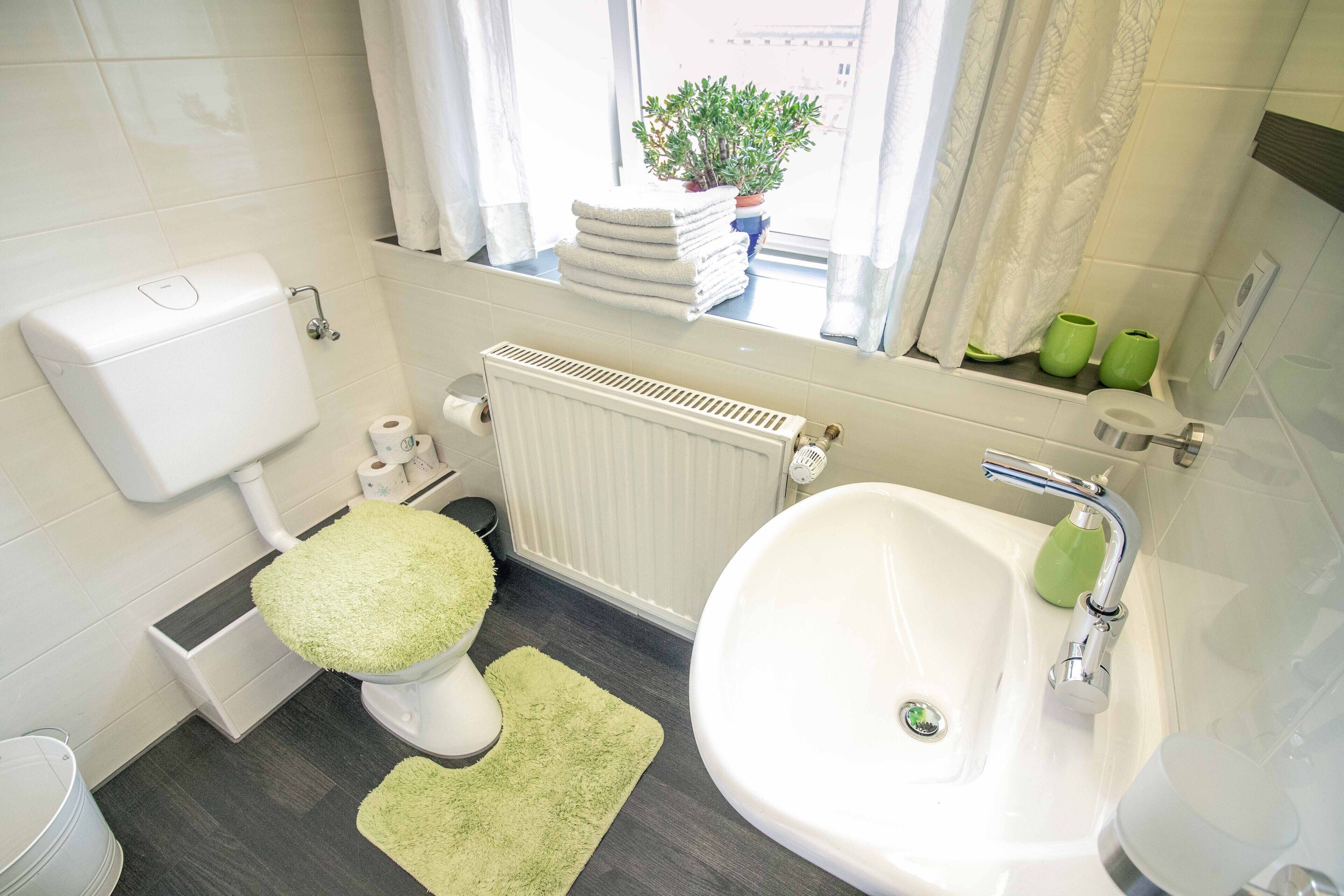 A bathroom with a toilet, bidet, sink, and a window with a view of a building and a plant.