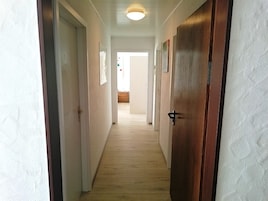 Um corredor estreito com piso de madeira e paredes brancas.