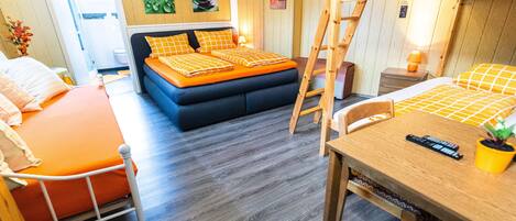 A room with a bunk bed, a sofa bed, a dining table, and a small kitchen area.