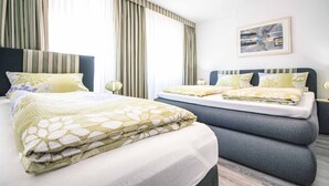 Een hotelkamer met twee bedden, een groot raam met gordijnen, een kroonluchter en een ingelijst schilderij aan de muur.