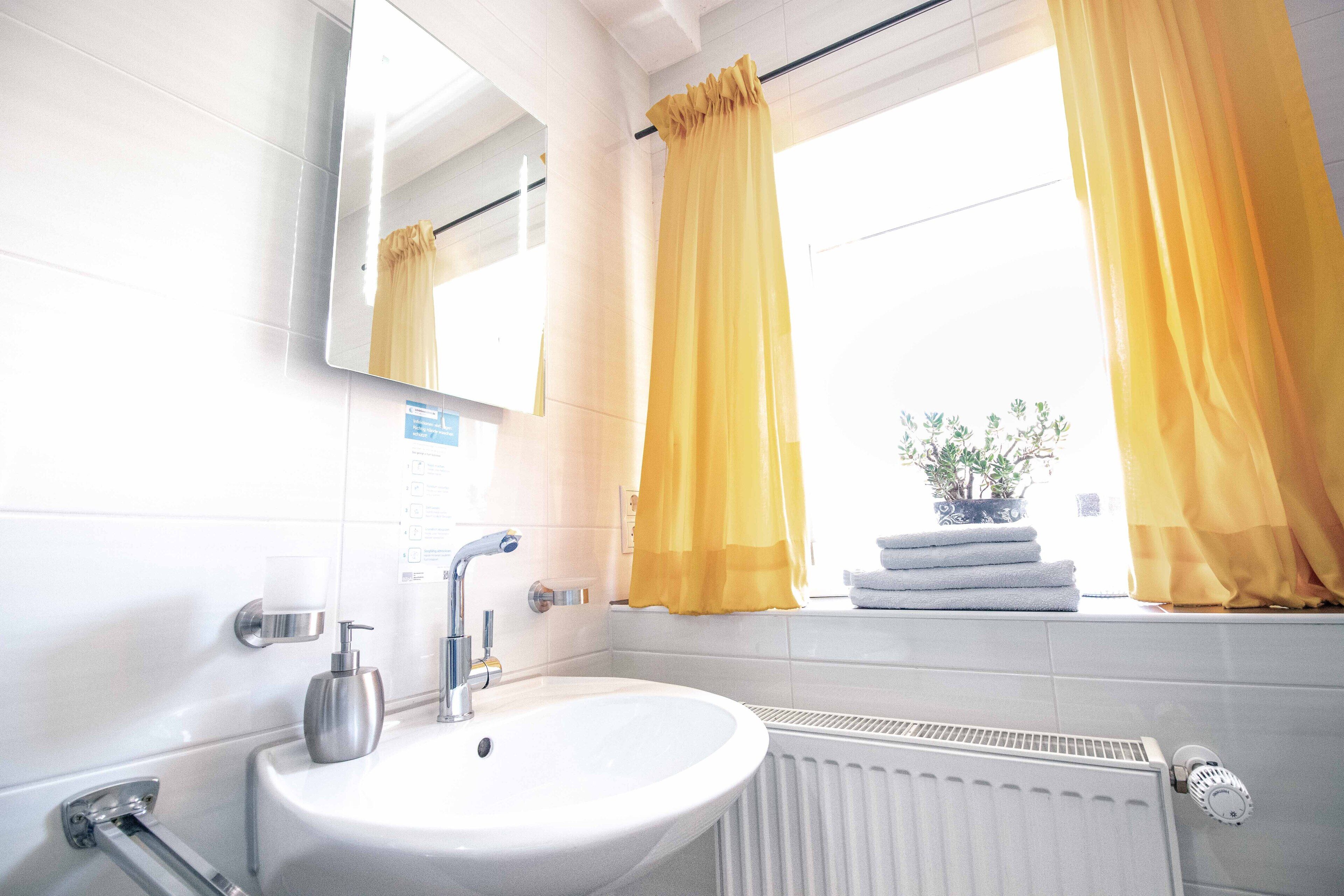 A bathroom with a white sink, mirror, and window with yellow curtains.