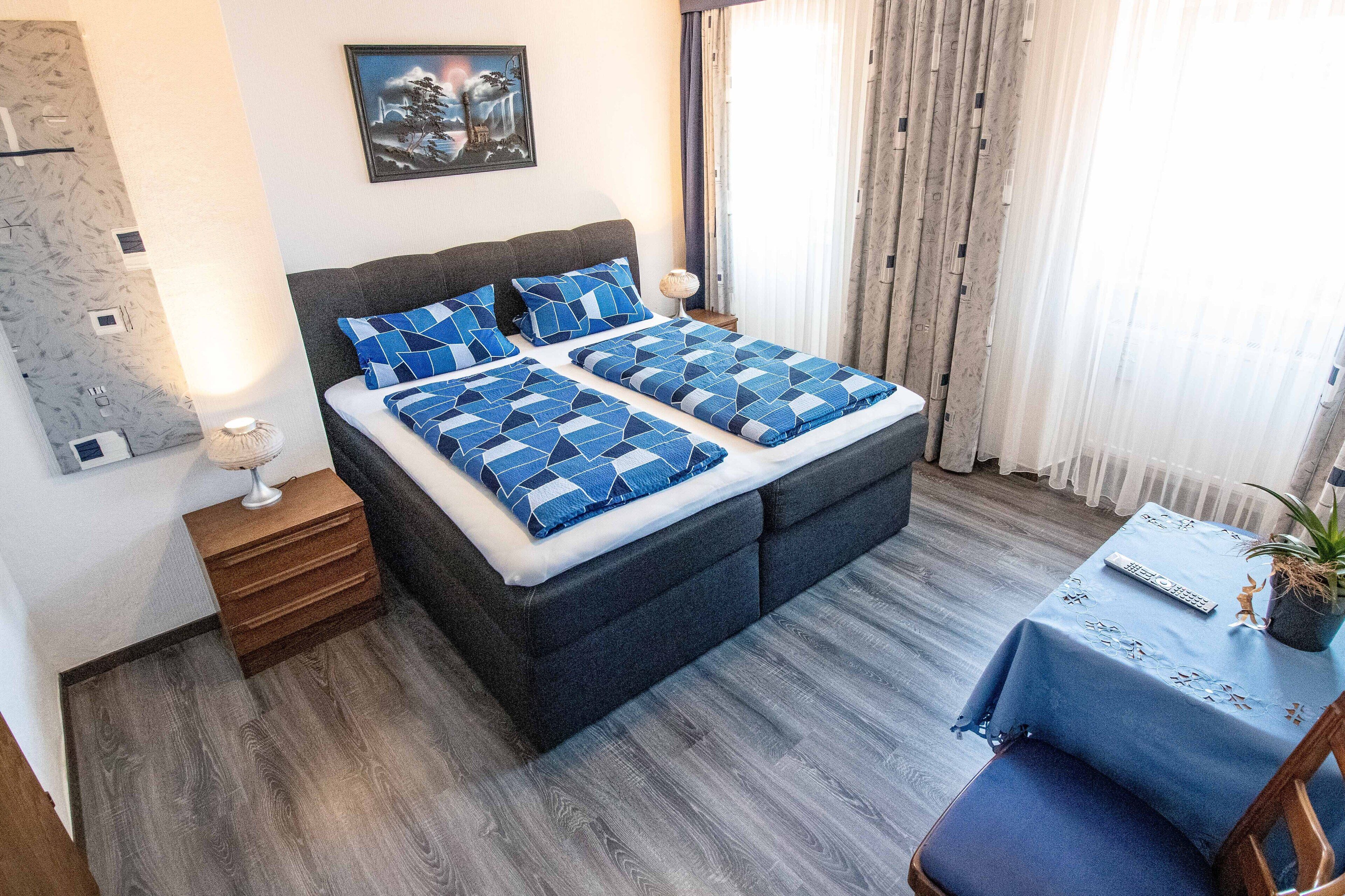 A bedroom with a bed, bedside tables, a chair, and a small table with a plant.