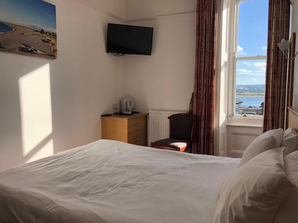 Ein Hotelzimmer mit Bett, Sessel, Fernseher, Fenster mit Blick und einem Bild an der Wand.