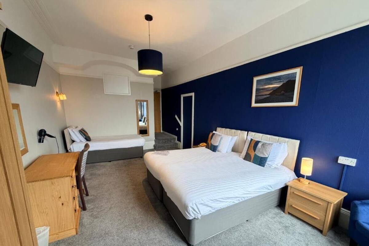 A bedroom with a bed, bedside tables, a desk, a chair, a TV, and a painting on the wall.